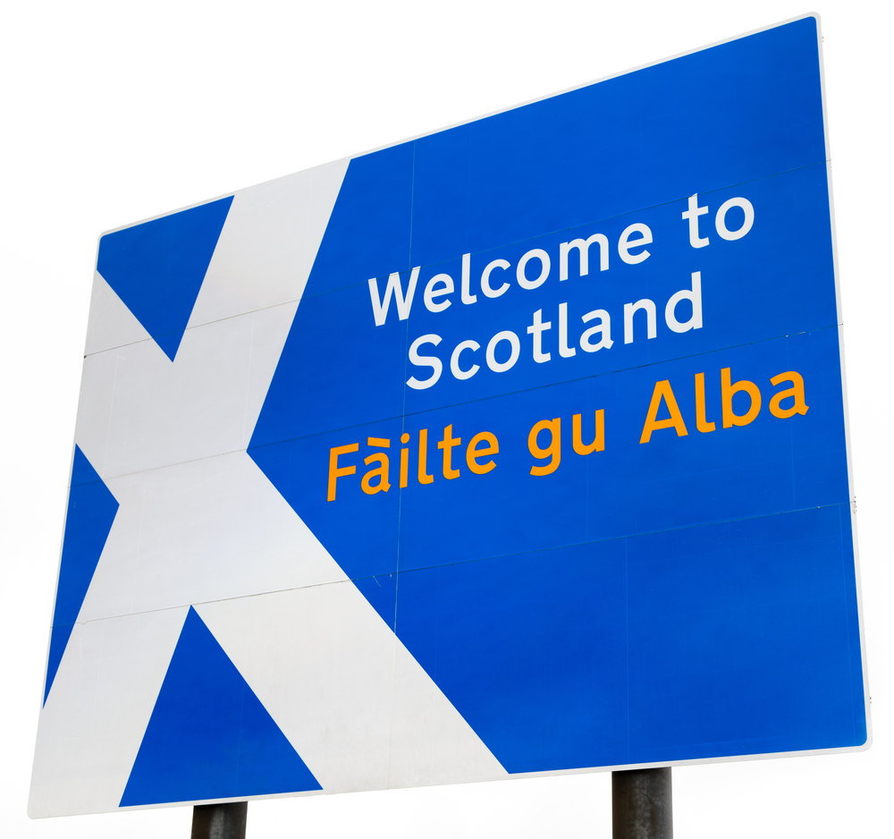 A sign on the border crossing to Scotland from England. Contains the Scottish flag and "Welcome to Scotland" in English and Gaelic. Isolated on a white background.